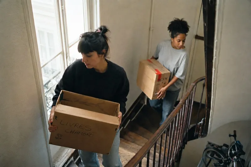 Deux étudiantes portant des cartons de déménagement dans un escalier parisien
